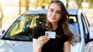 Woman holding driving licence near car.